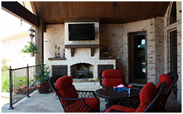 Custom outdoor living space built by CCH Pools a custom pool builder in Longview, Texas. Red chairs around a table against a white brick fireplace with an outdoor TV above