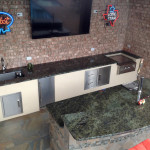 outdoor kitchen bar with TV, neon beer signs and stainless steel appliances