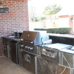 decoratively tiled outdoor kitchen with stainless steel appliances against red brick home